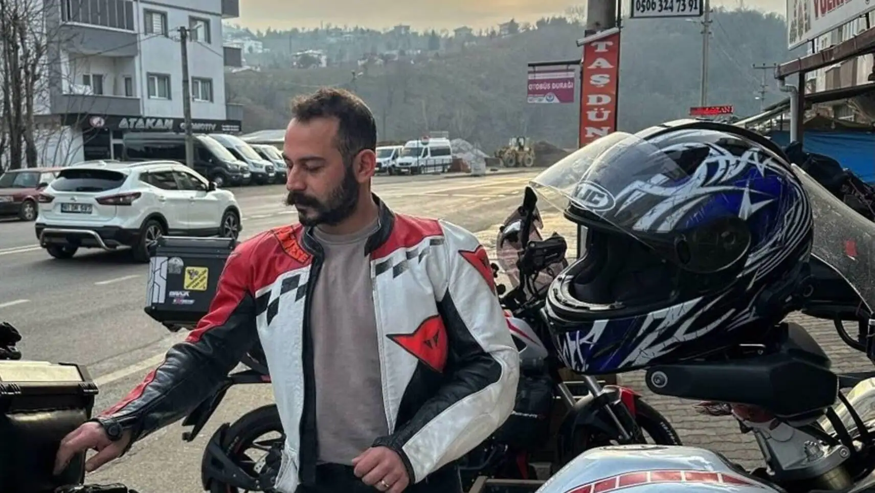Bir adam motosikletinin yanında duruyor.