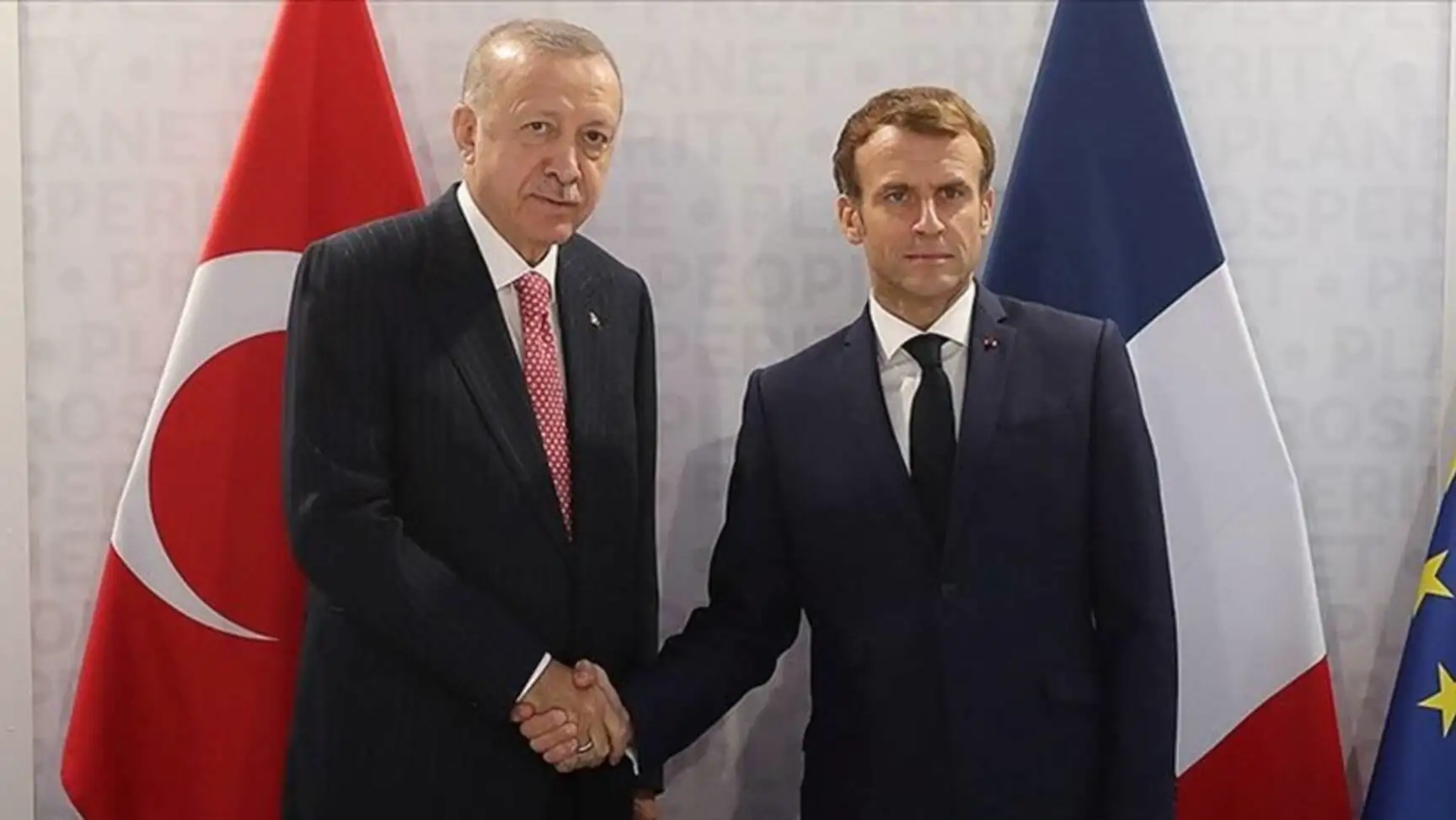 President Erdoğan and Macron shaking hands in front of flags. President Erdoğan and Macron shaking hands in front of flags.