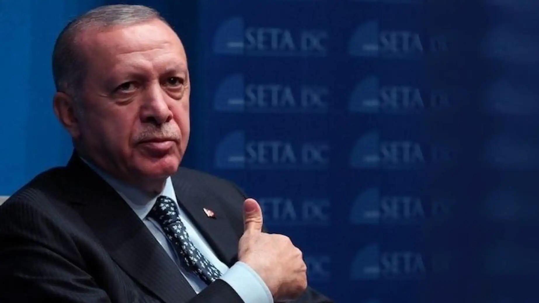 Bir adam takım elbise içinde baş parmağını yukarı kaldırıyor.