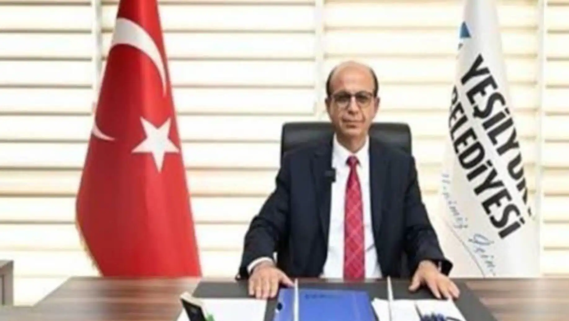 A man sitting at a desk with flags behind him. A man sitting at a desk with flags behind him.