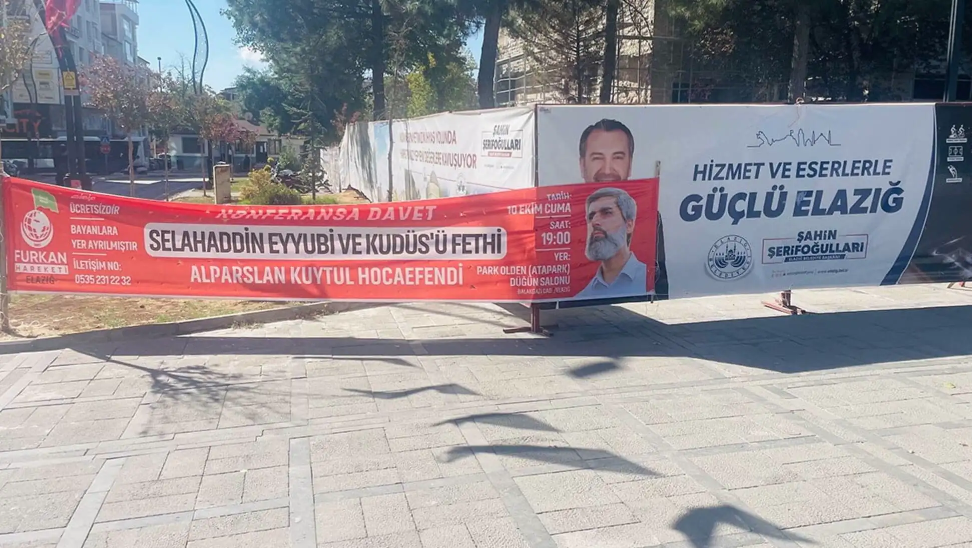 Furkan Vakfı üyesi bir adam, afişle duruyor.
