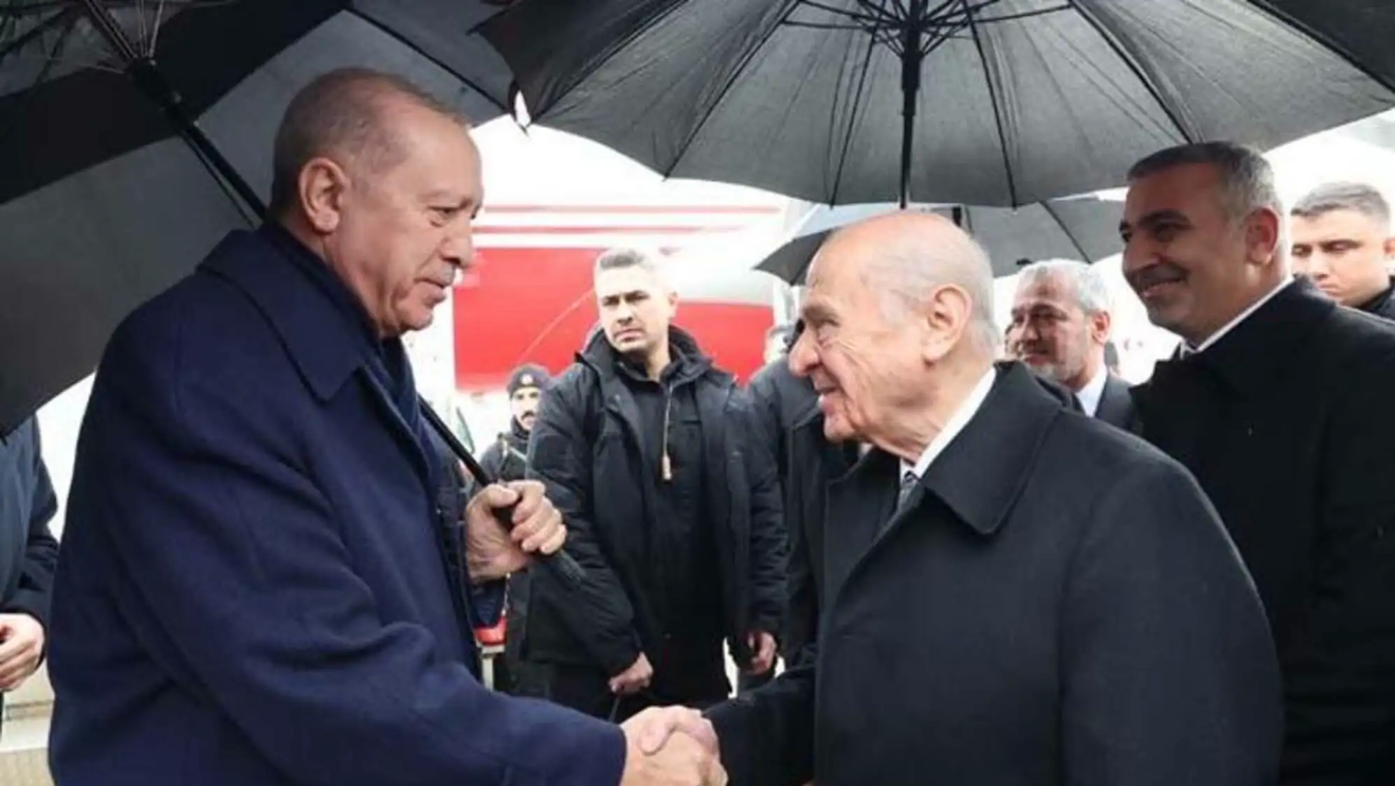 A group of men shaking hands under umbrellas.