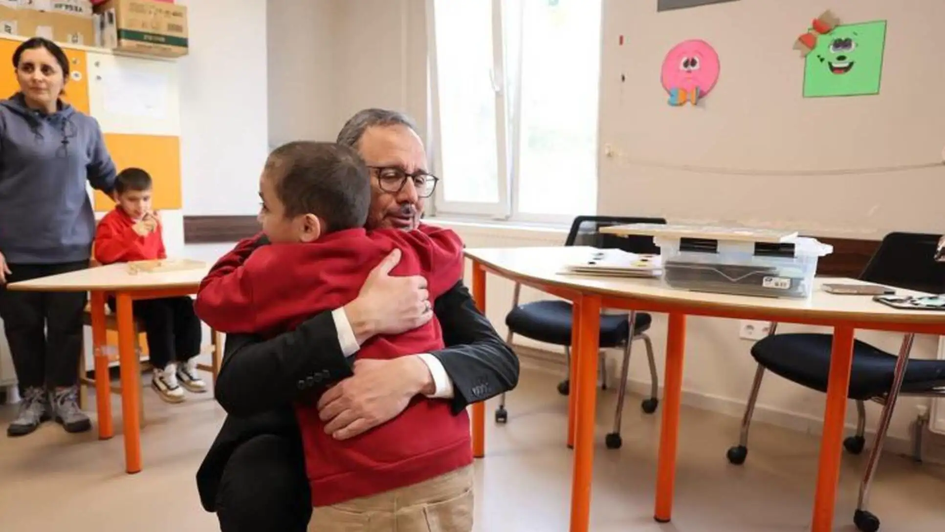 A man hugging a boy in a classroom.