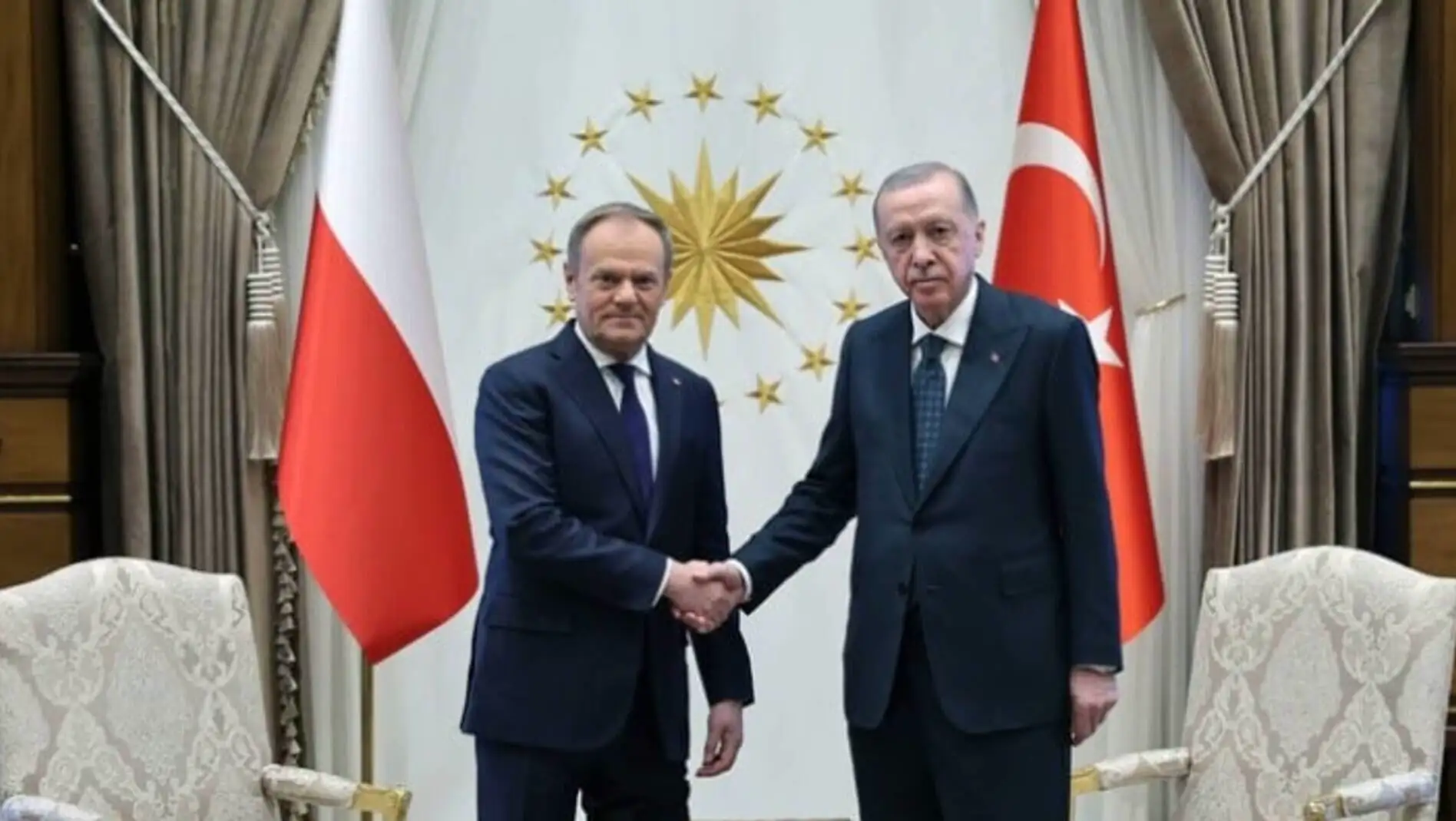 Two men shaking hands in front of flags.