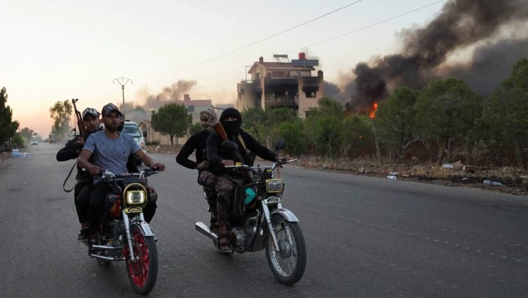 A group of people riding motorcycles on a road with a building behind them. A group of people riding motorcycles on a road with a building behind them.