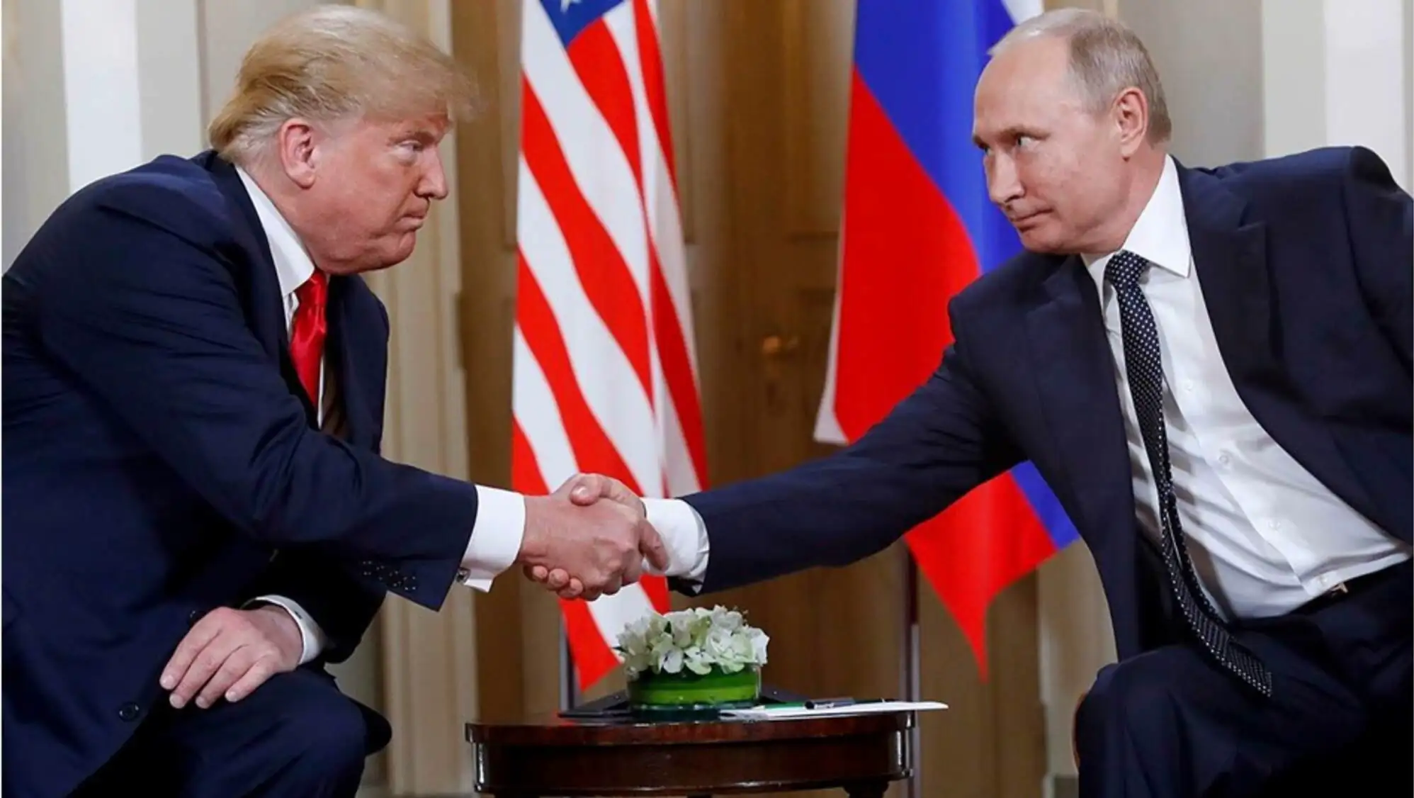 Two men shaking hands in front of flags.
