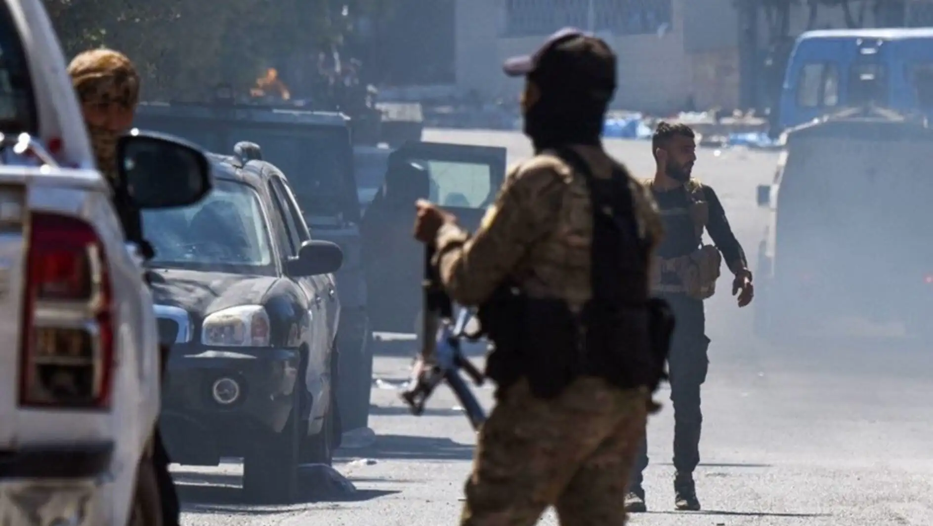 A man in military uniform holding a gun in front of a car. A man in military uniform holding a gun in front of a car.