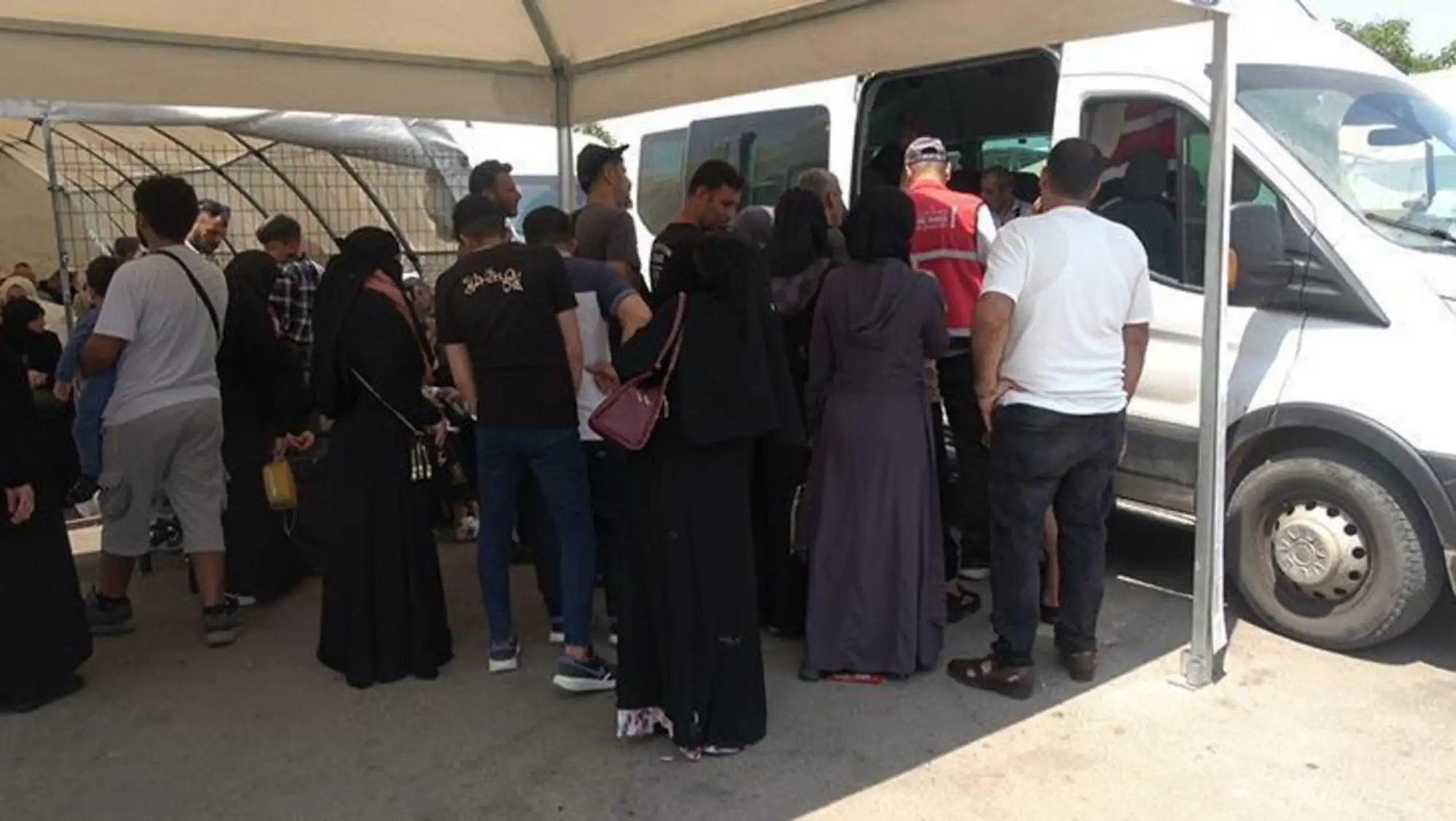 A group of people standing in line with their belongings. A group of people standing in line with their belongings.