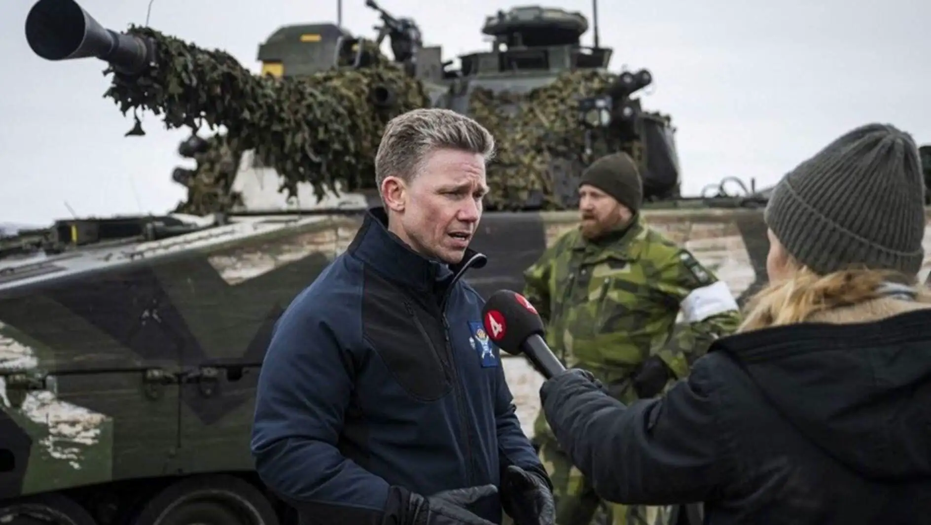 A man in military uniform holding a gun and standing in front of a military vehicle.