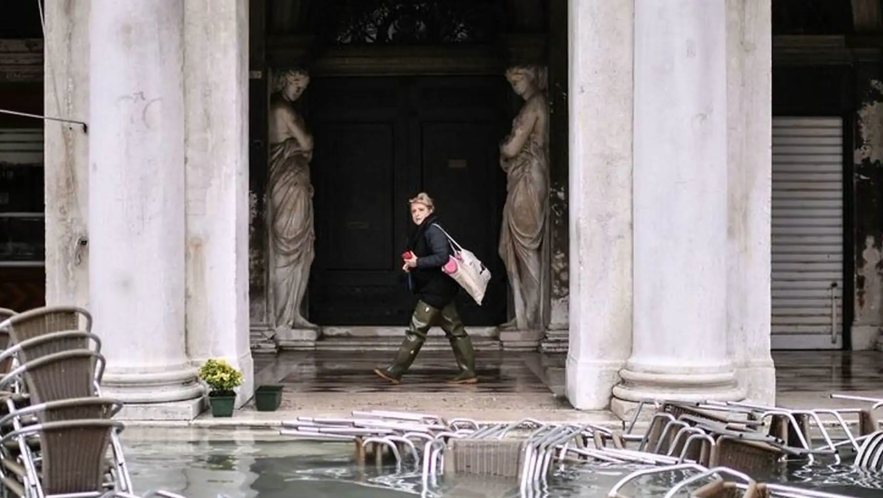 A woman walking in front of a building with chairs and statues. A woman walking in front of a building with chairs and statues.