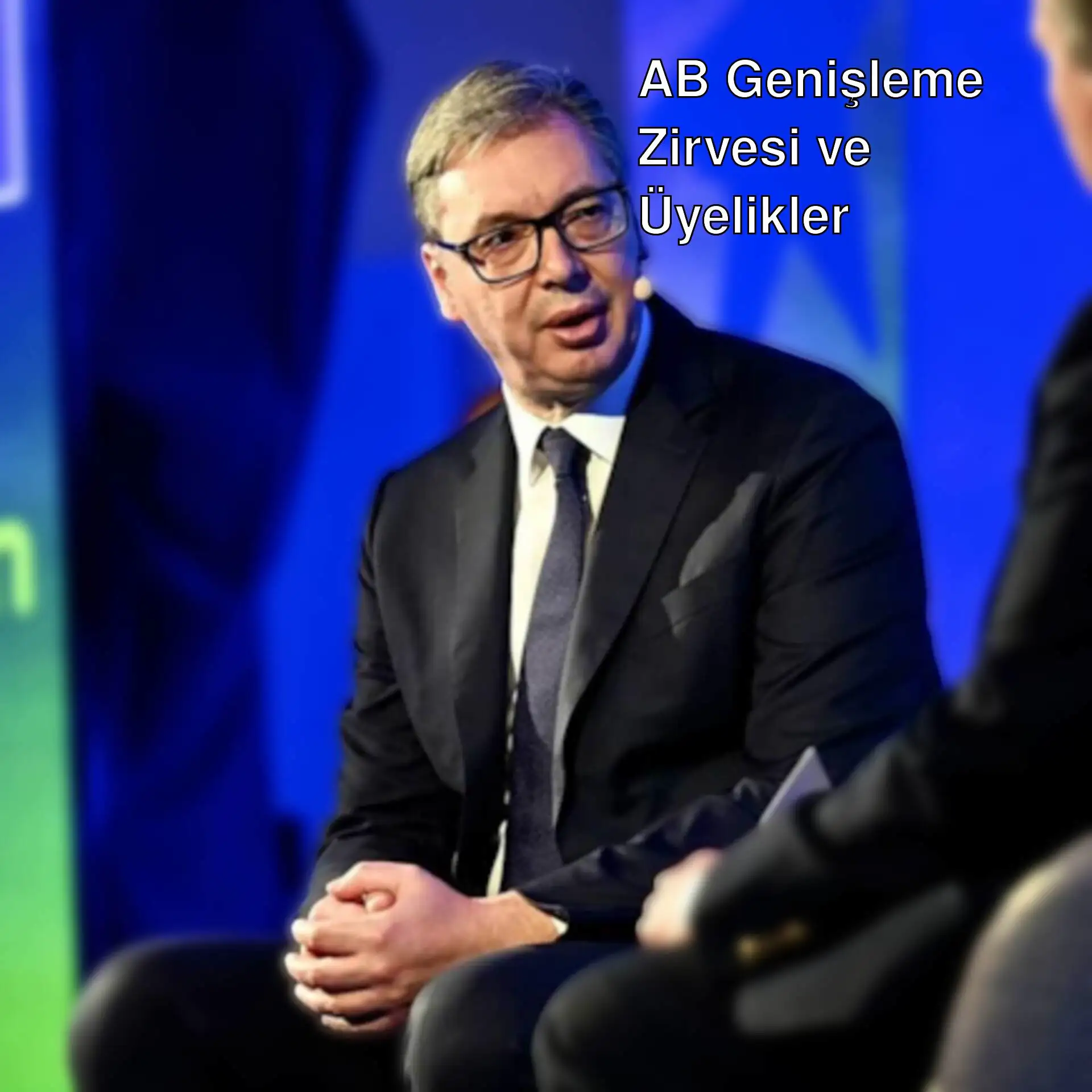 Bir adam takım elbise giymiş ve diğer bir adamla konuşuyor.