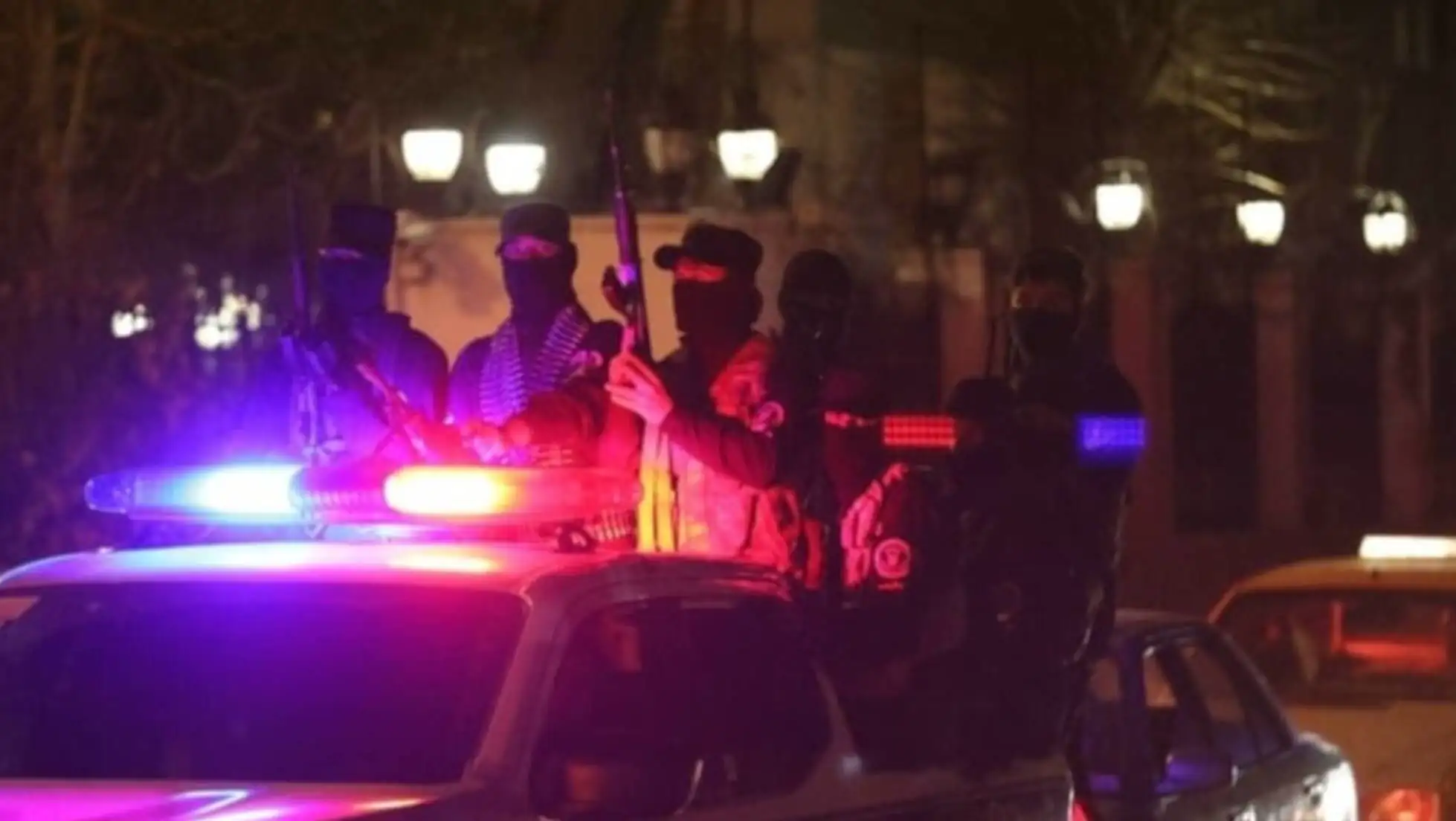 A group of masked individuals holding guns on top of a car.