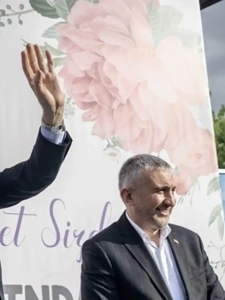 Bir adam takım elbise ile el sallıyor.