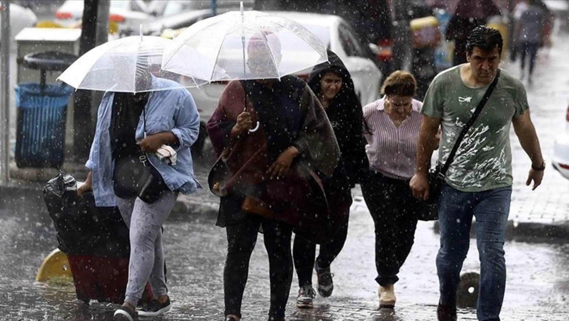 Bir grup insan yağmur altında şemsiye tutarak yürüyor. Bir grup insan yağmur altında şemsiye tutarak yürüyor.