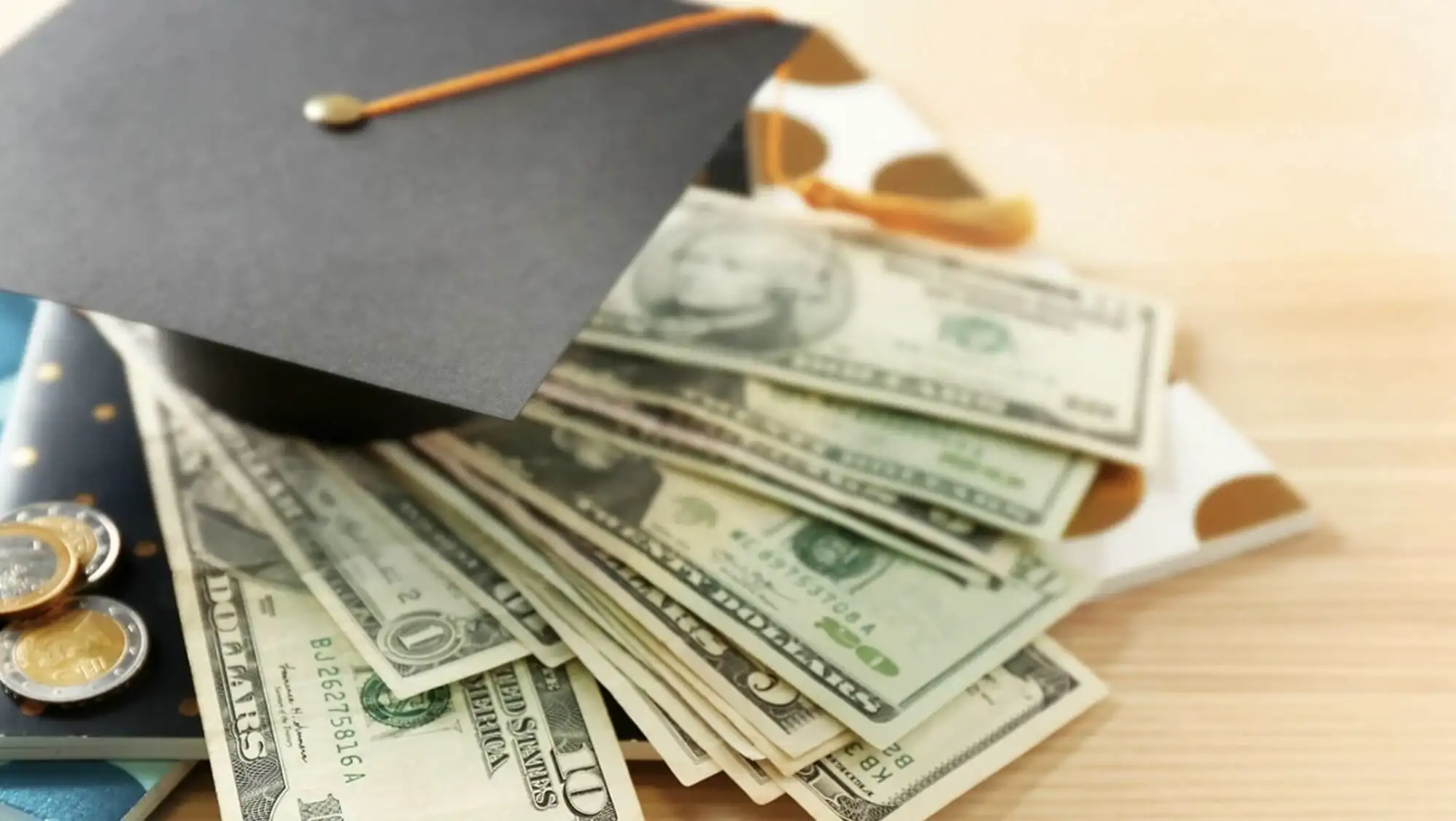 A graduation cap and money on a table. A graduation cap and money on a table.