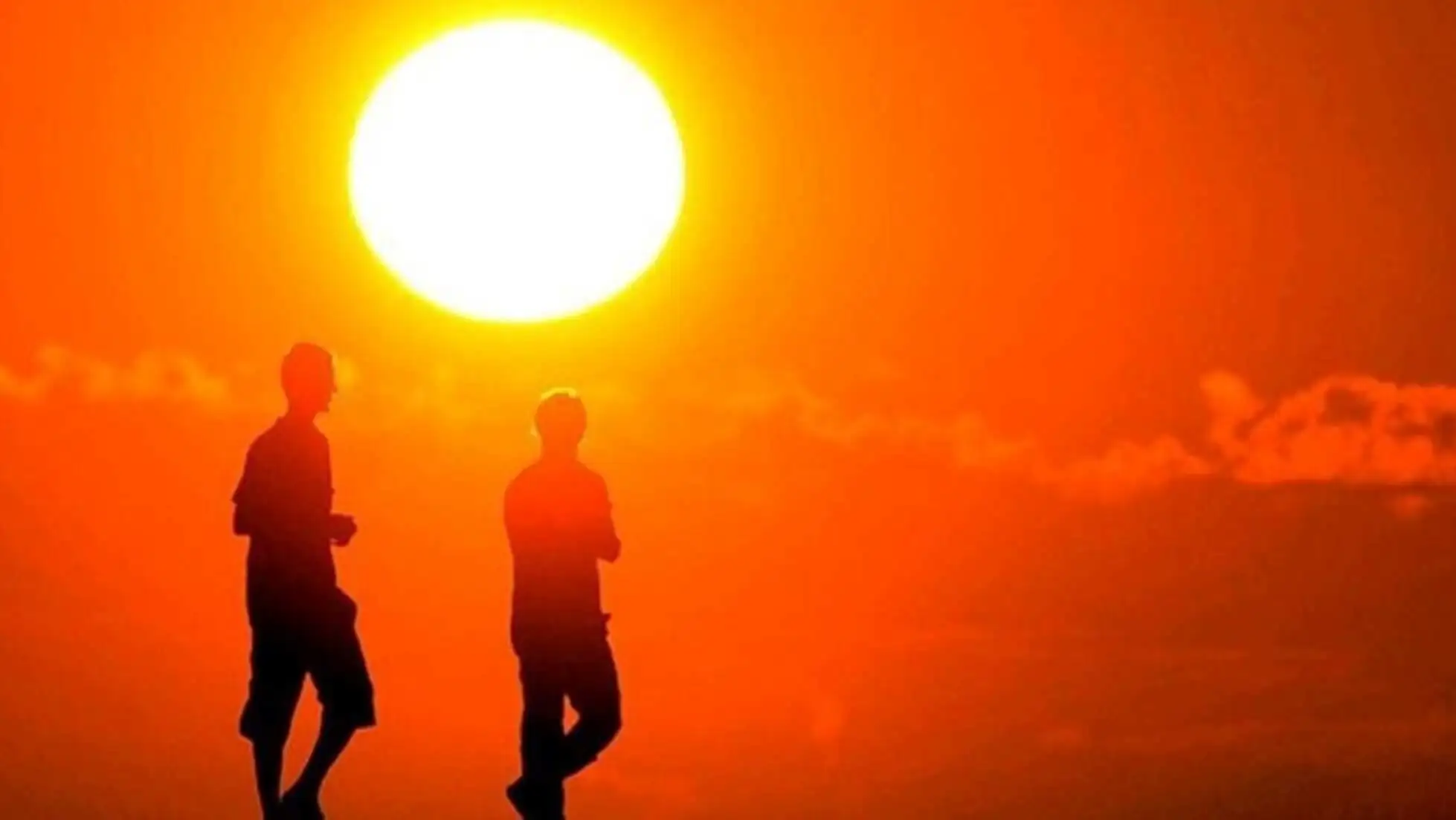 A group of people running in front of a bright sun.
