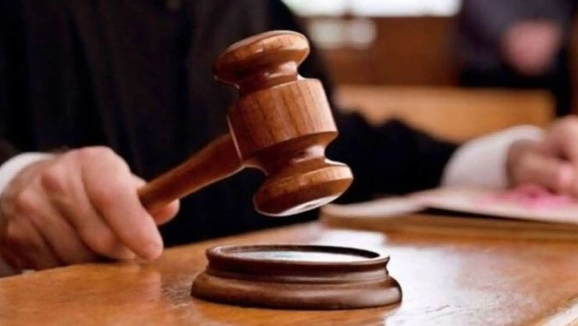 A hand holding a gavel over a wooden surface. A hand holding a gavel over a wooden surface.