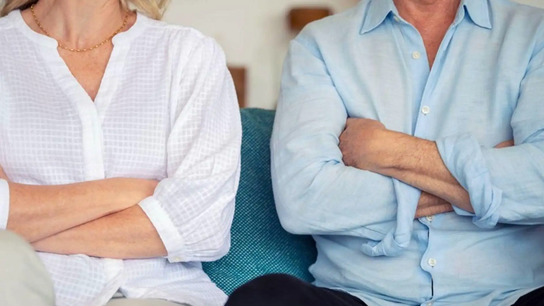 A man and woman sitting on a couch with their arms crossed.