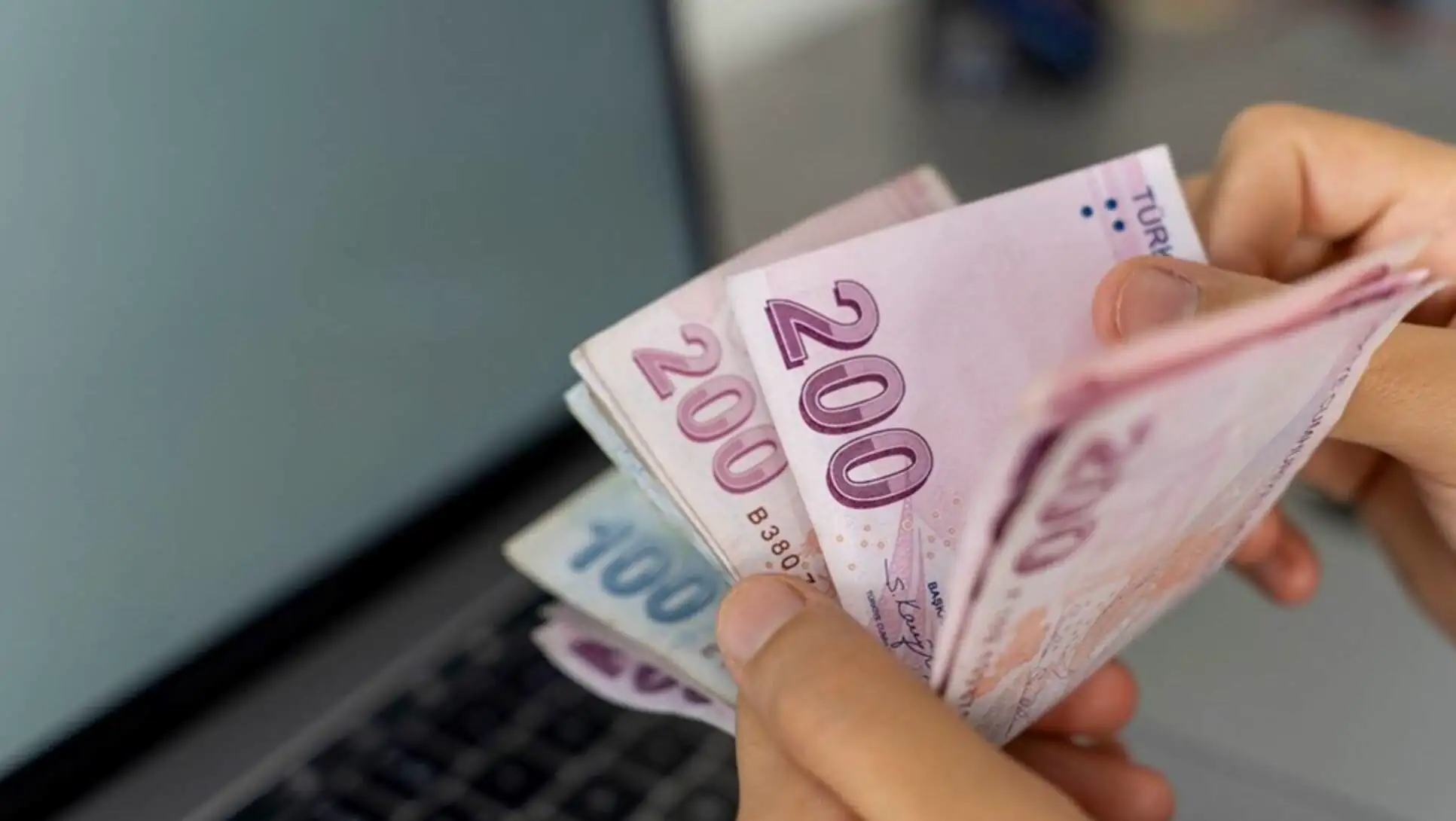 A hand holding money in front of a laptop. A hand holding money in front of a laptop.