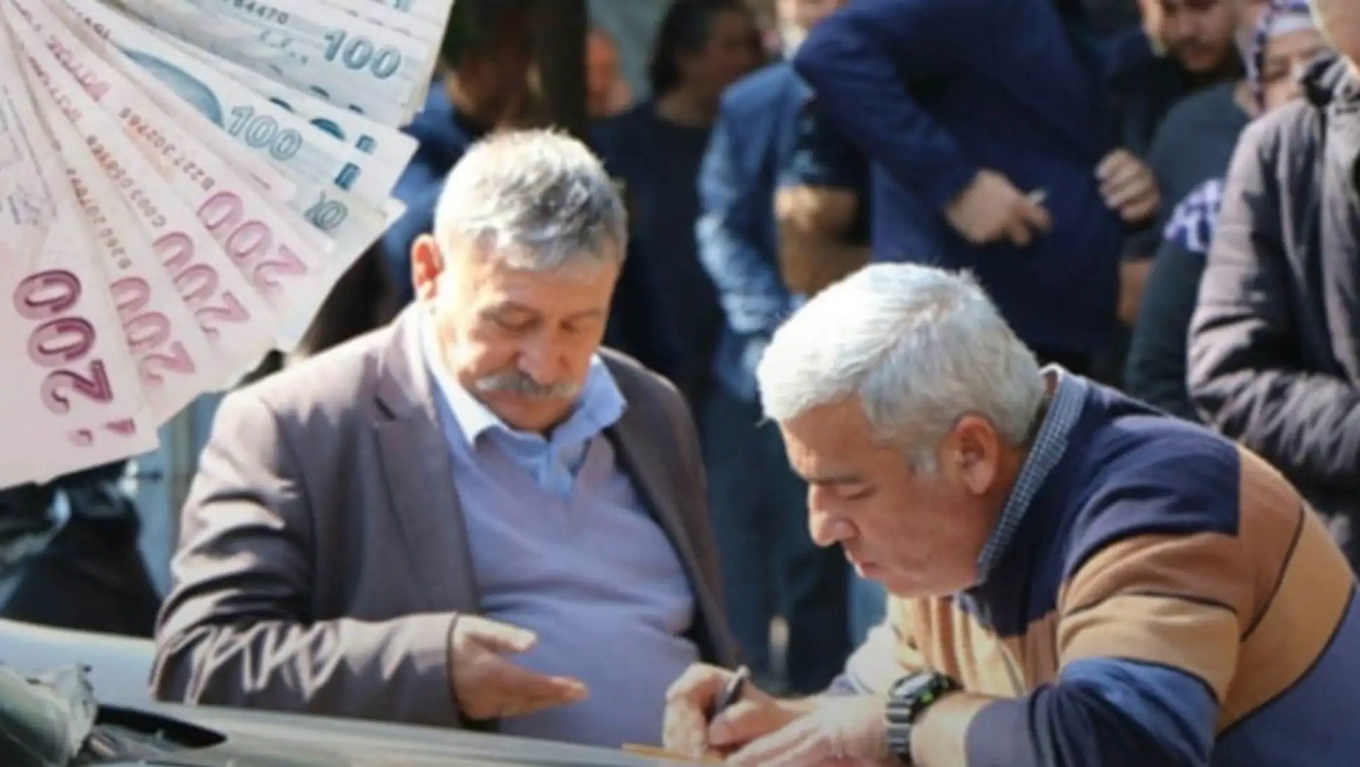A man signing a document with another man standing behind him.