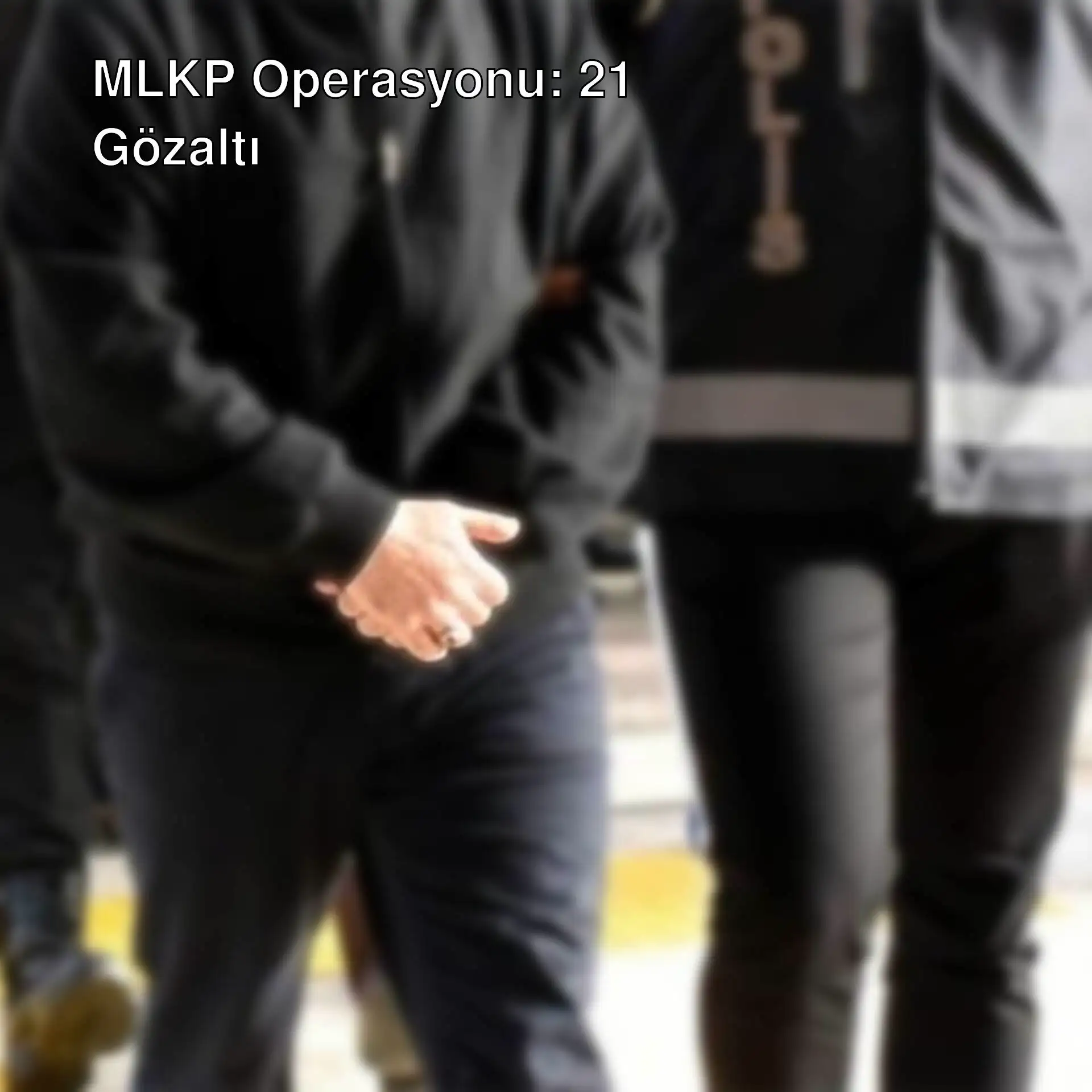 Bir adam siyah ceket ve pantolonla polis memuruyla yürüyor.