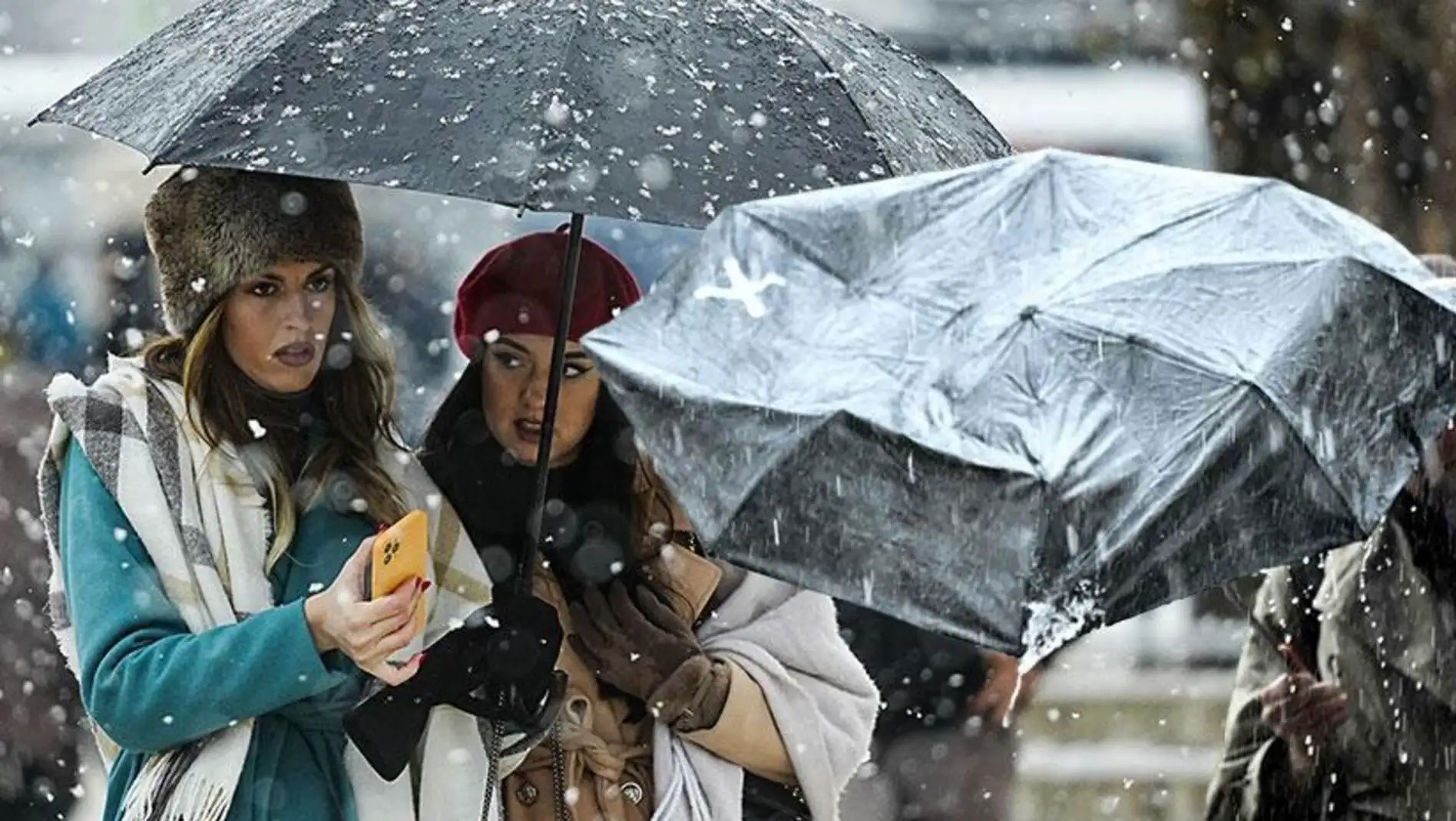 Two women walking under an umbrella in the snow.