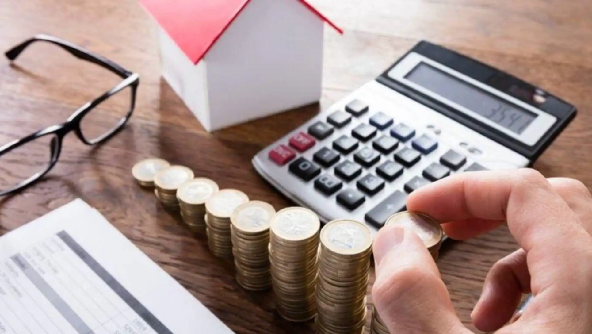 A hand stacking coins next to a calculator.