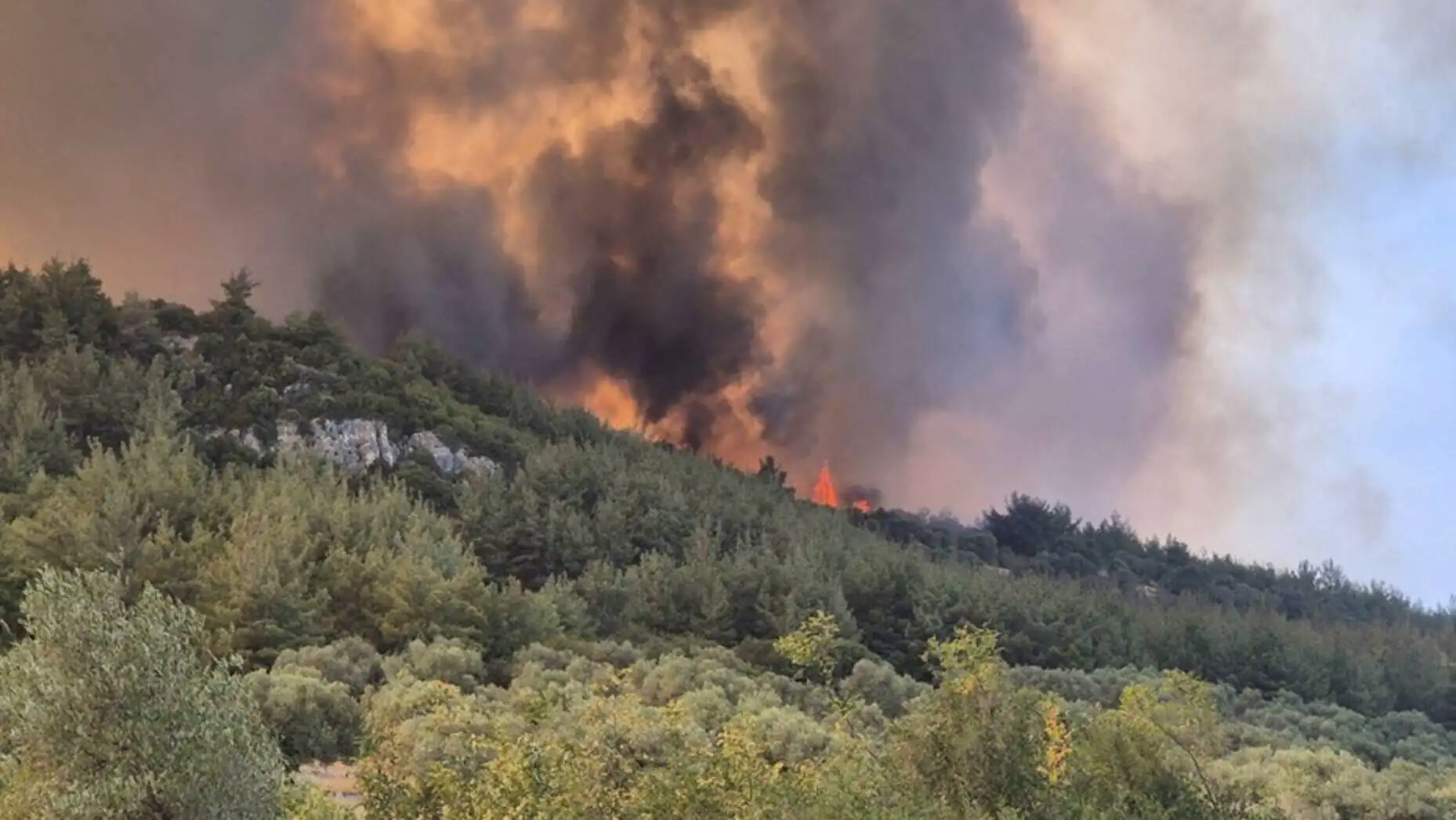A forest fire with smoke coming out of the mountains