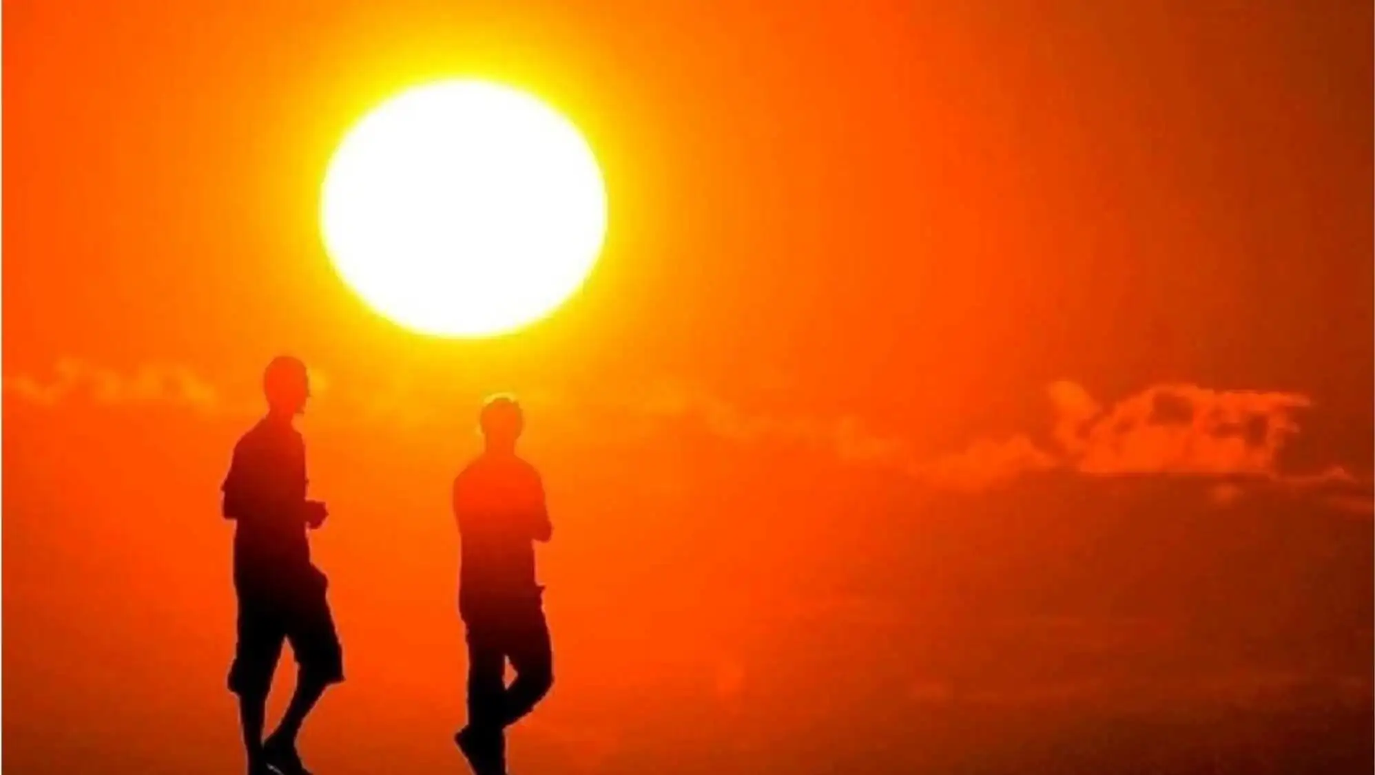 A group of people running in front of a bright sun.
