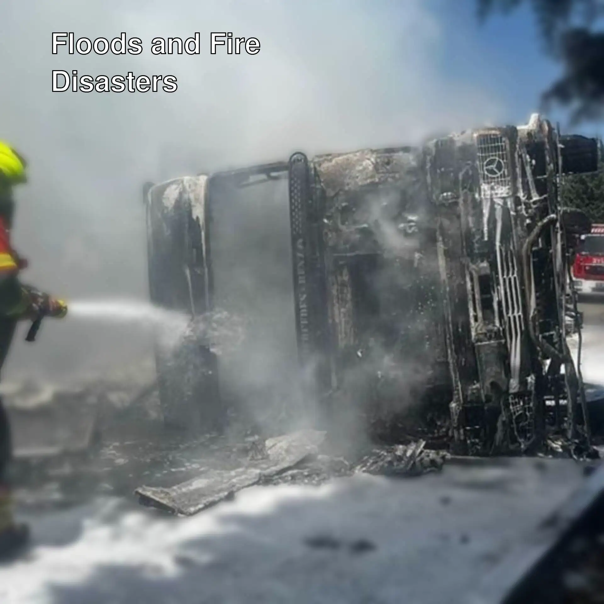 A firefighter spraying water onto a burnt vehicle.