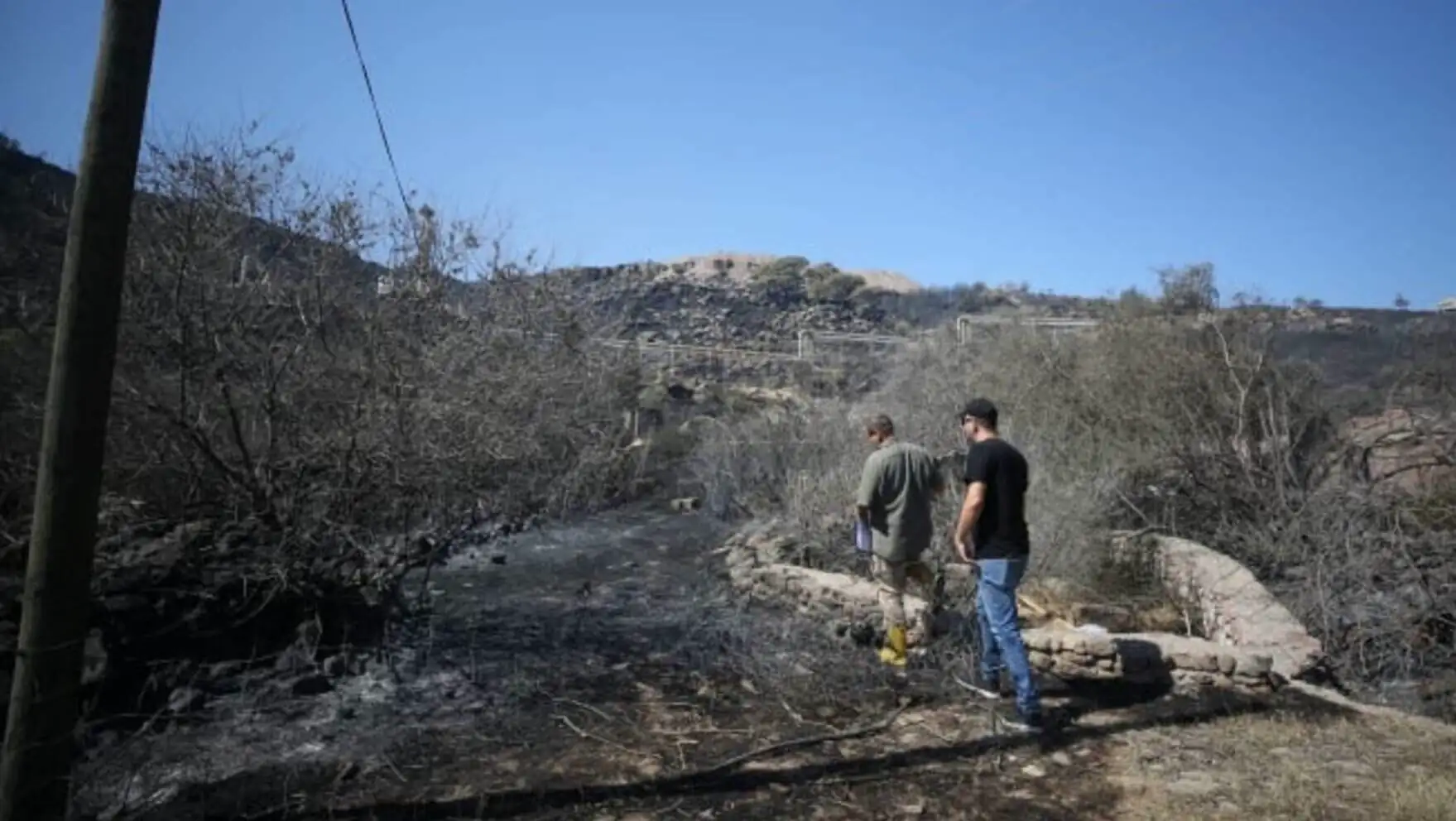 A couple of men standing near a burned area.