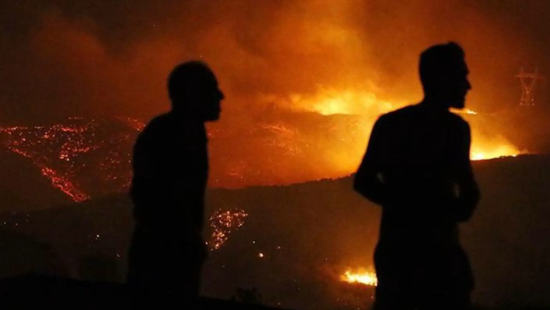 A silhouette of men looking at a forest fire.