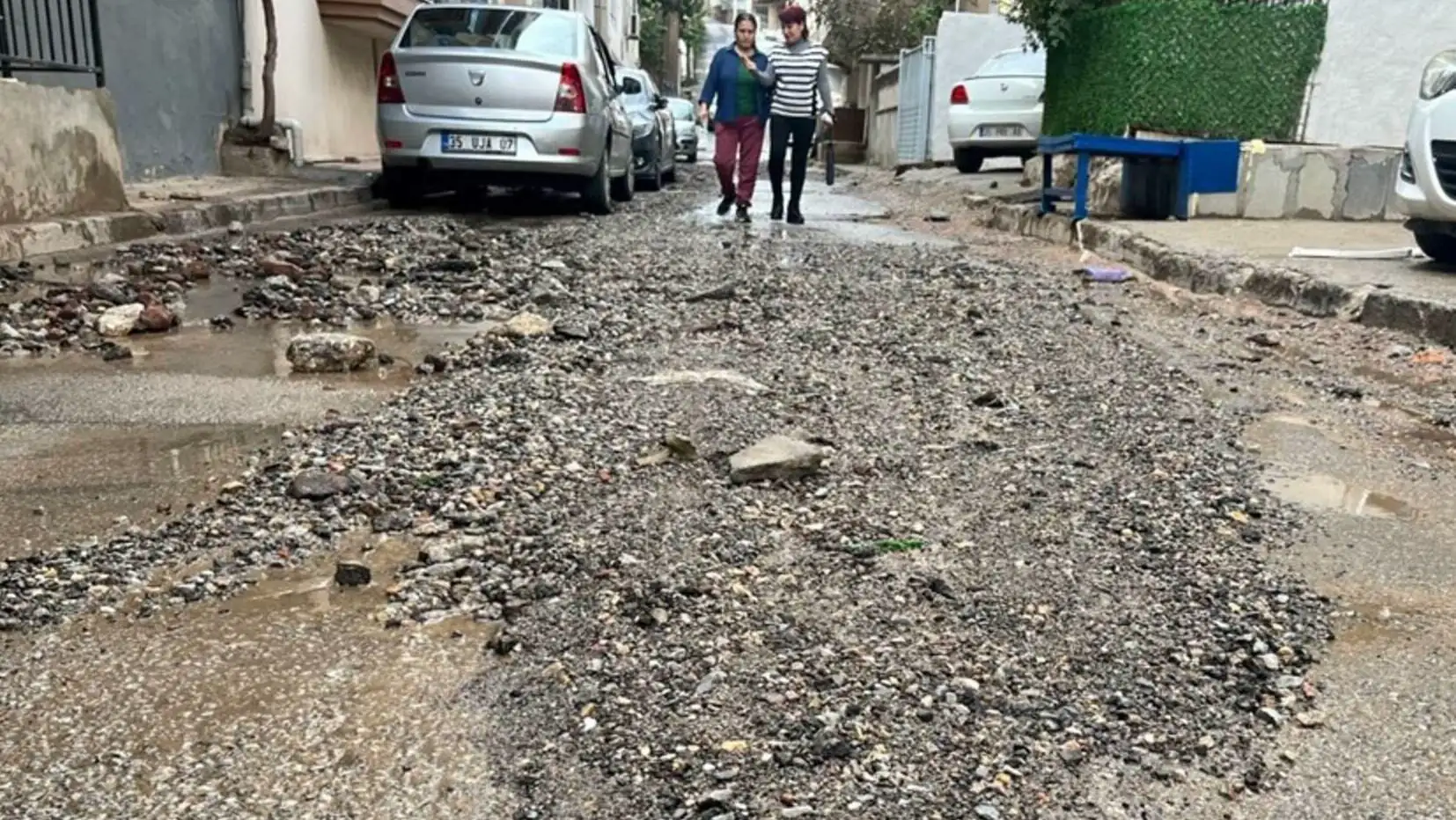 Islak bir caddede yürüyen birkaç kişi.