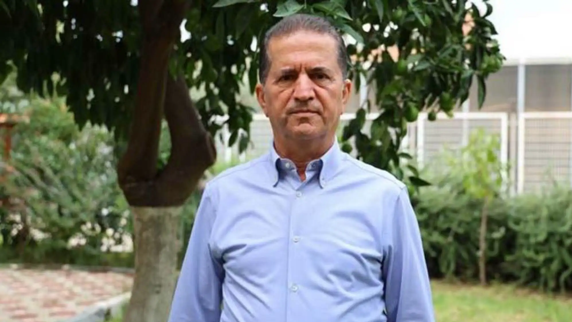 Bir adam mavi bir gömlekle dışarıda duruyor.