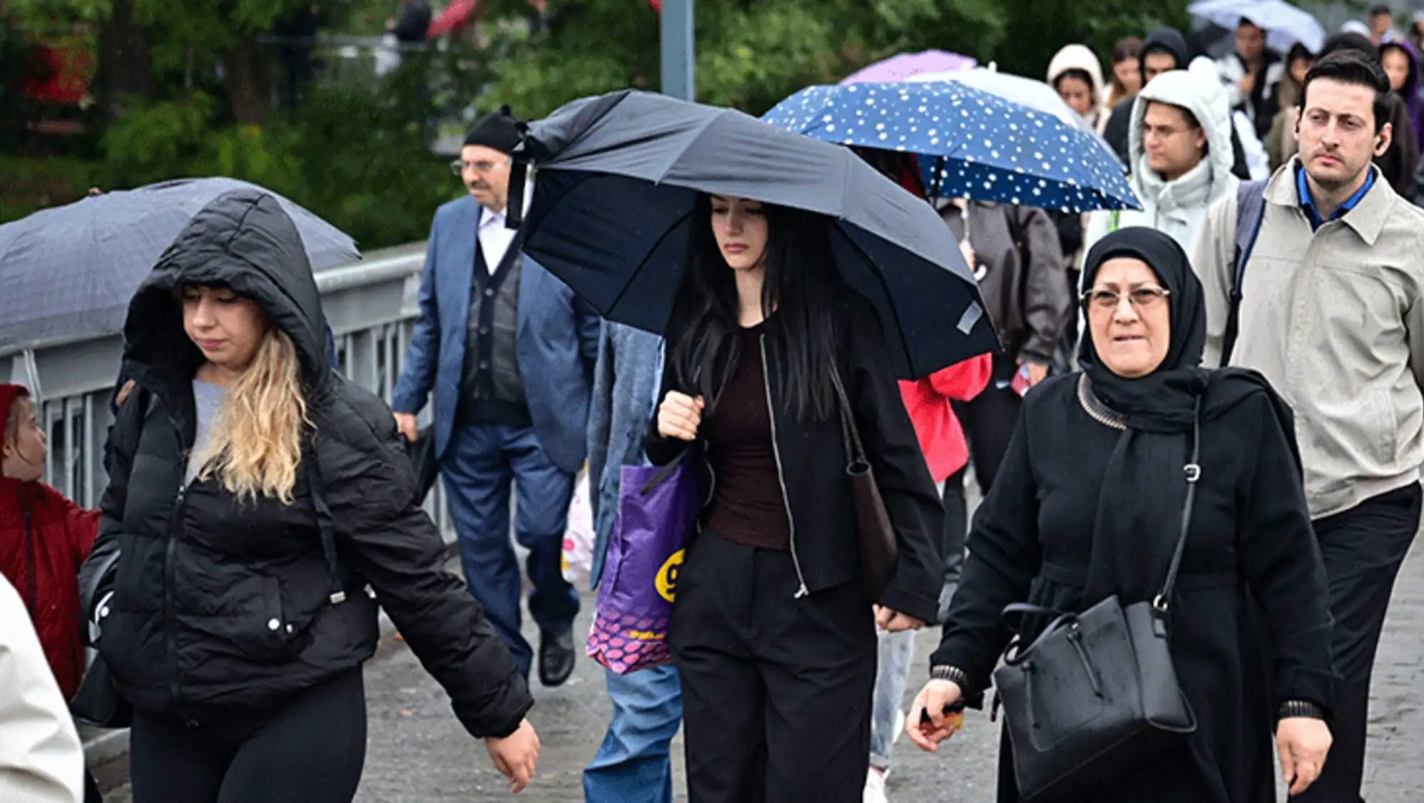 Bir grup insan yağmurda şemsiye tutarak yürüyor.