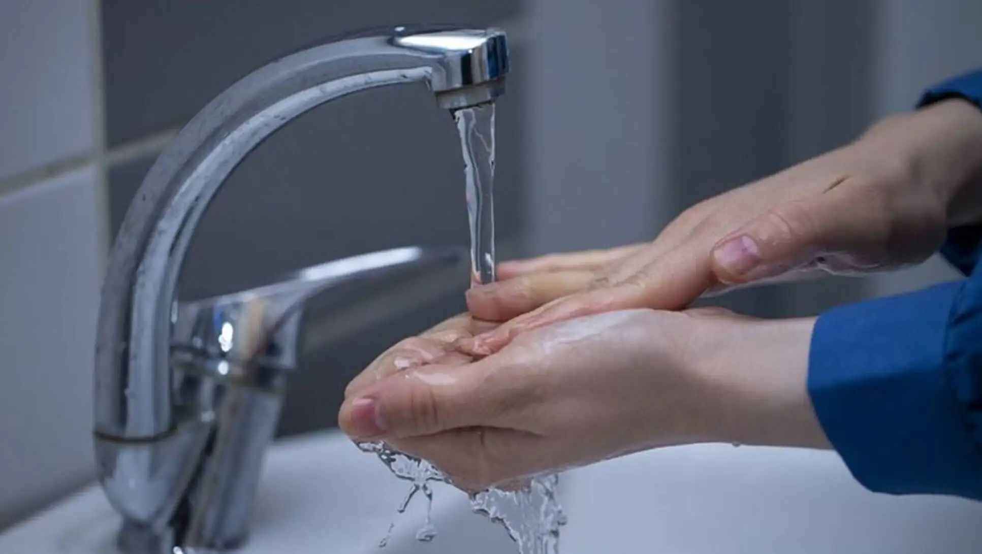 A person washing their hands under a running water faucet. A person washing their hands under a running water faucet.