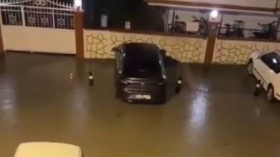 Bir kişi, sel nedeniyle su dolmuş bir otoparkta diz çökerek çalışıyor. Bir kişi, sel nedeniyle su dolmuş bir otoparkta diz çökerek çalışıyor.