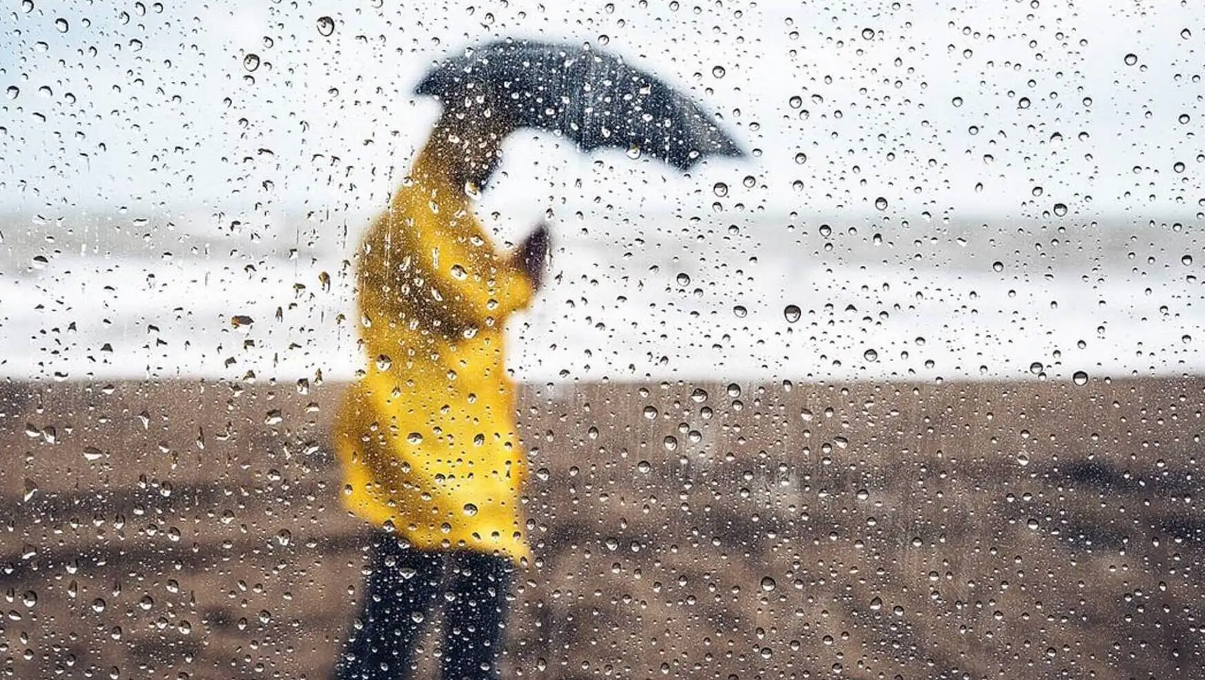 A person in a yellow raincoat holding an umbrella. A person in a yellow raincoat holding an umbrella.