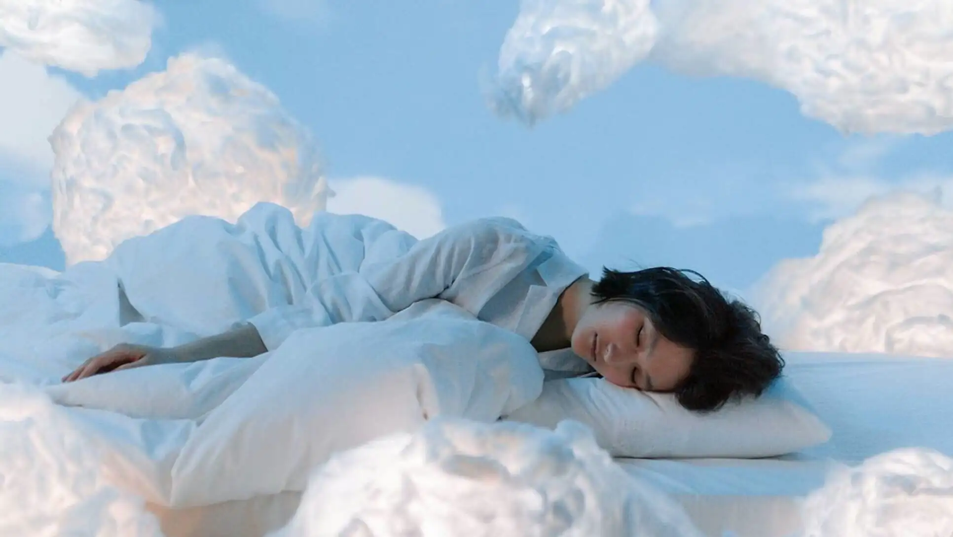 A woman lying in bed with clouds of white clouds.