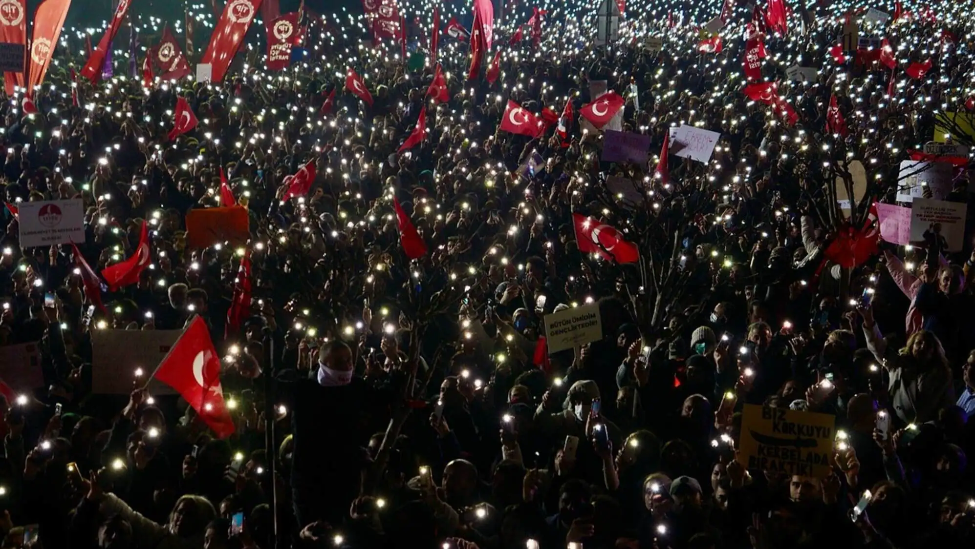Kalabalık bir grup insan bayraklarla yürüyüş yapıyor.