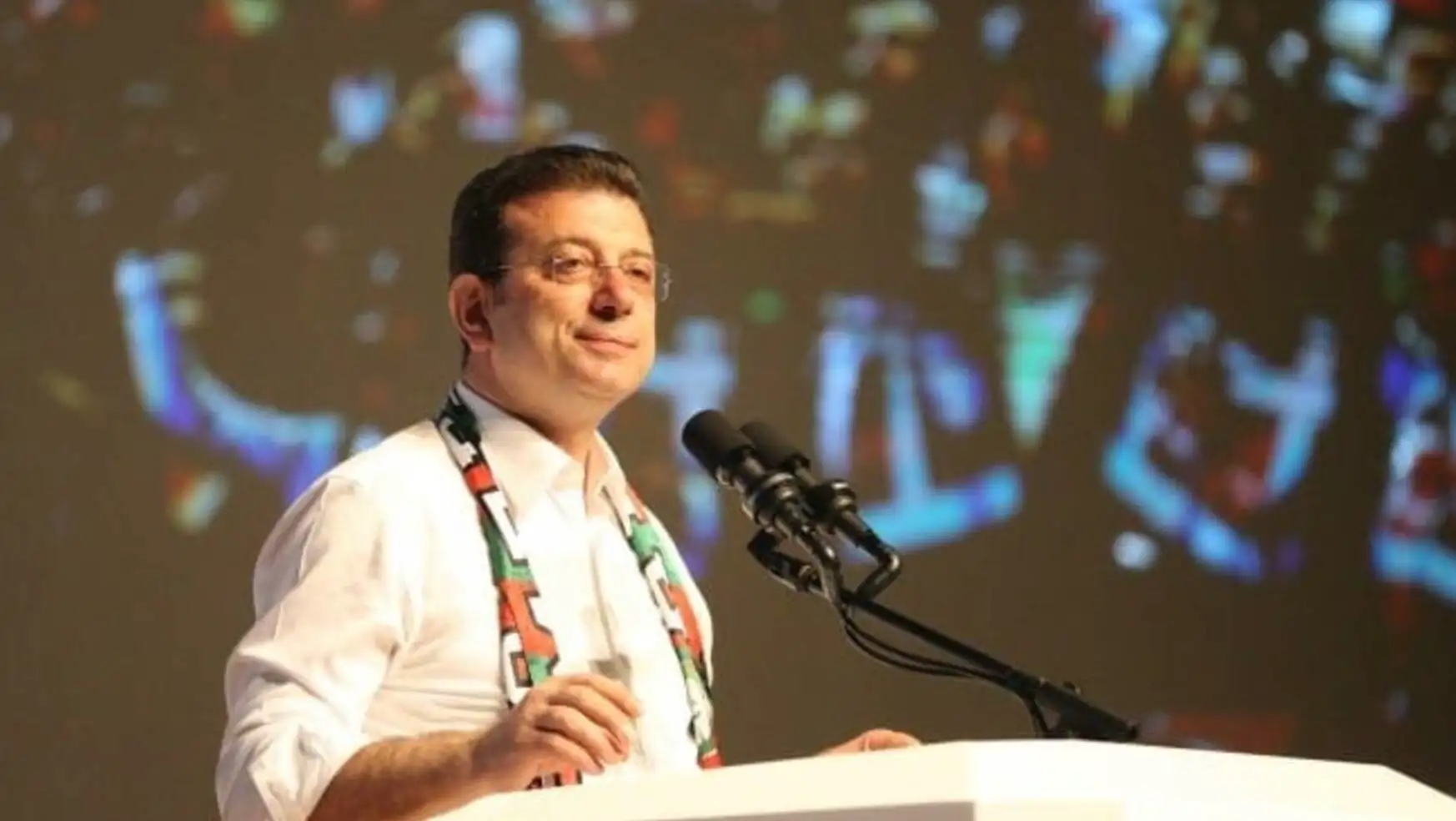 Ekrem İmamoğlu bir podiumda mikrofonla konuşuyor. Ekrem İmamoğlu bir podiumda mikrofonla konuşuyor.