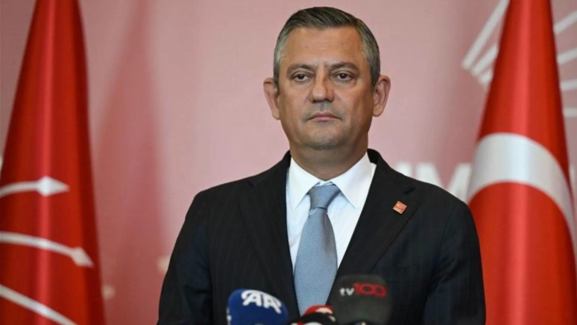 Bir adam takım elbise giymiş ve mikrofonların önünde duruyor.
