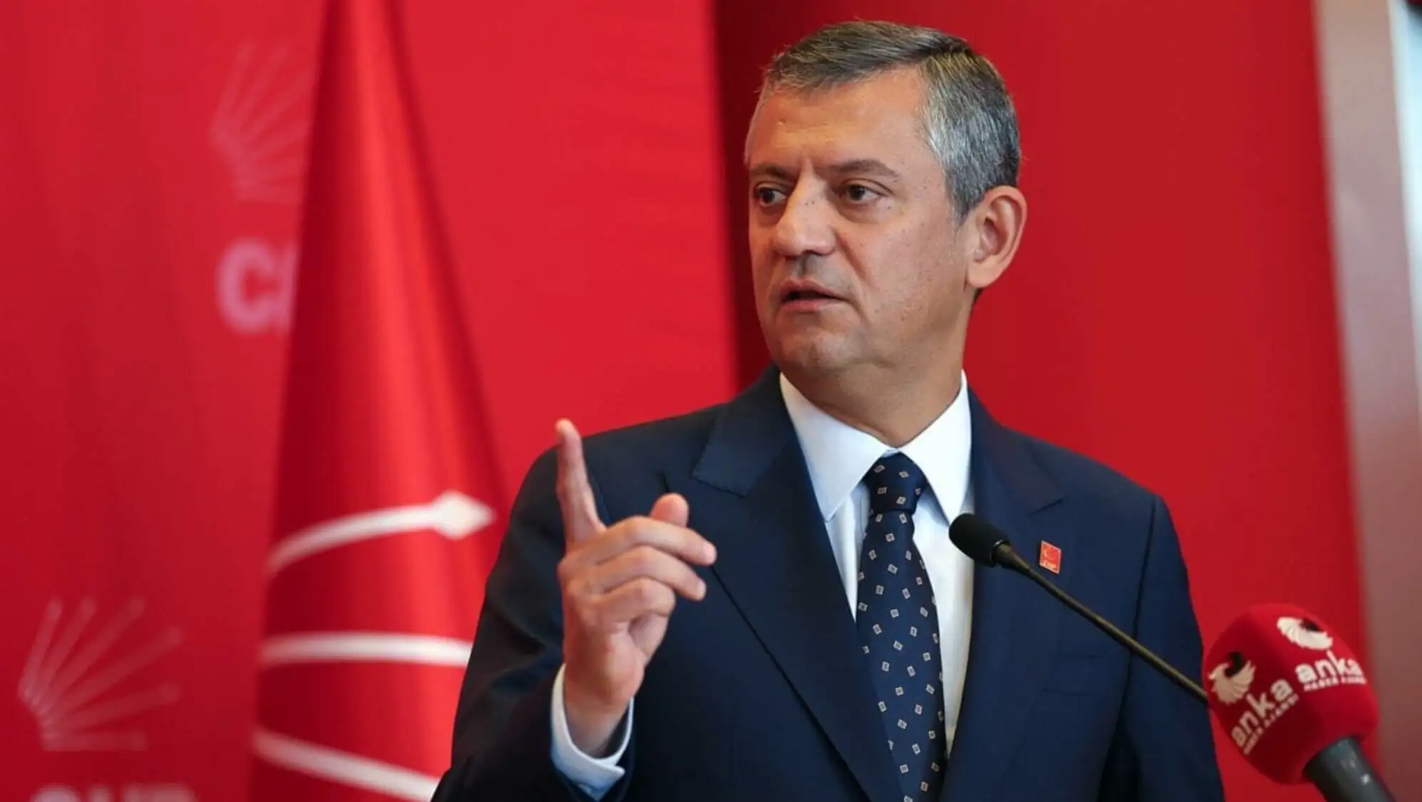 Mikrofonun önünde bir adam takım elbise giymiş.