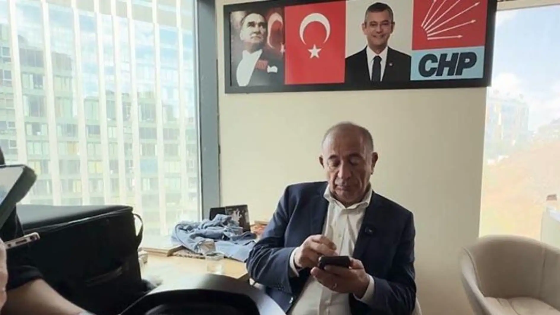 Gürsel Tekin sitting at a desk looking at his phone. Gürsel Tekin sitting at a desk looking at his phone.