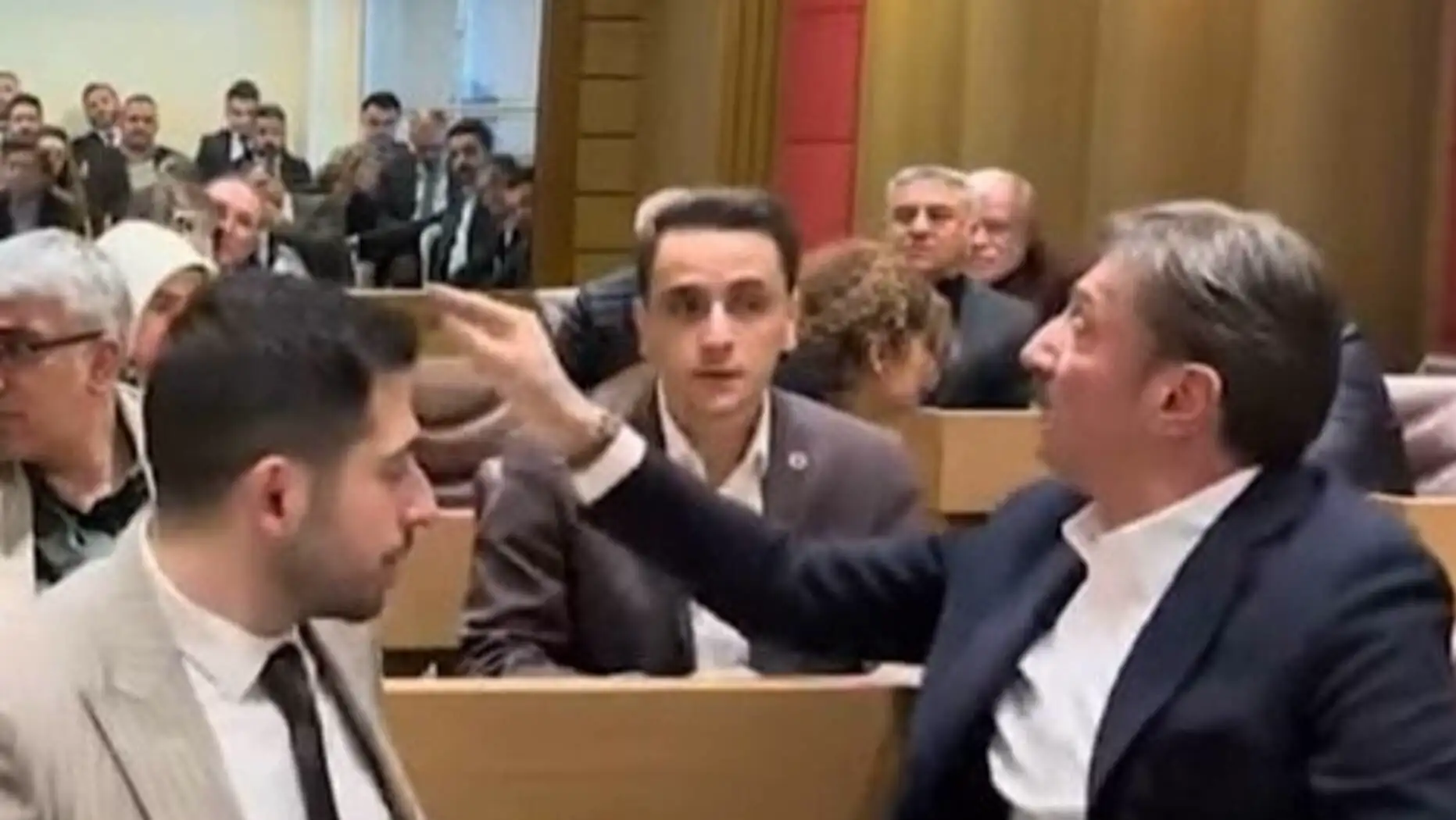 Bir adam podiumda başka bir adama işaret ediyor.